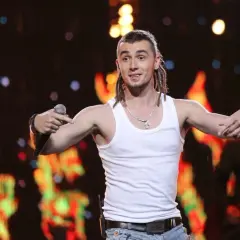 Kamil Bednarek w białej podkoszulce śpiewa na koncercie.