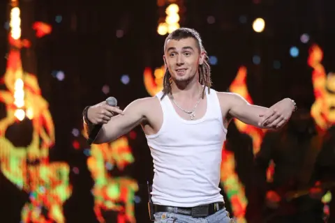 Kamil Bednarek w białej podkoszulce śpiewa na koncercie.