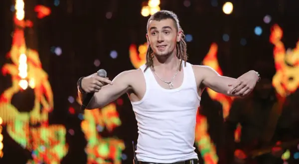 Kamil Bednarek w białej podkoszulce śpiewa na koncercie.